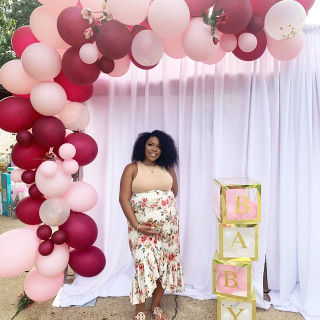 Woman standing under a pink and red balloon arch with 'Baby' blocks in the background