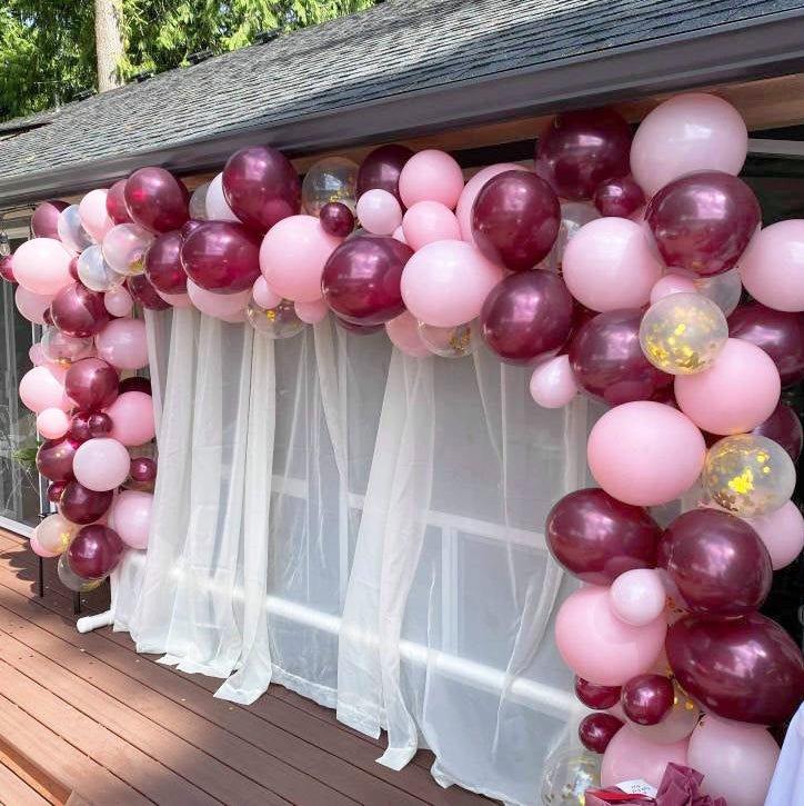 Balloon arch with pink and purple balloons in front of a window