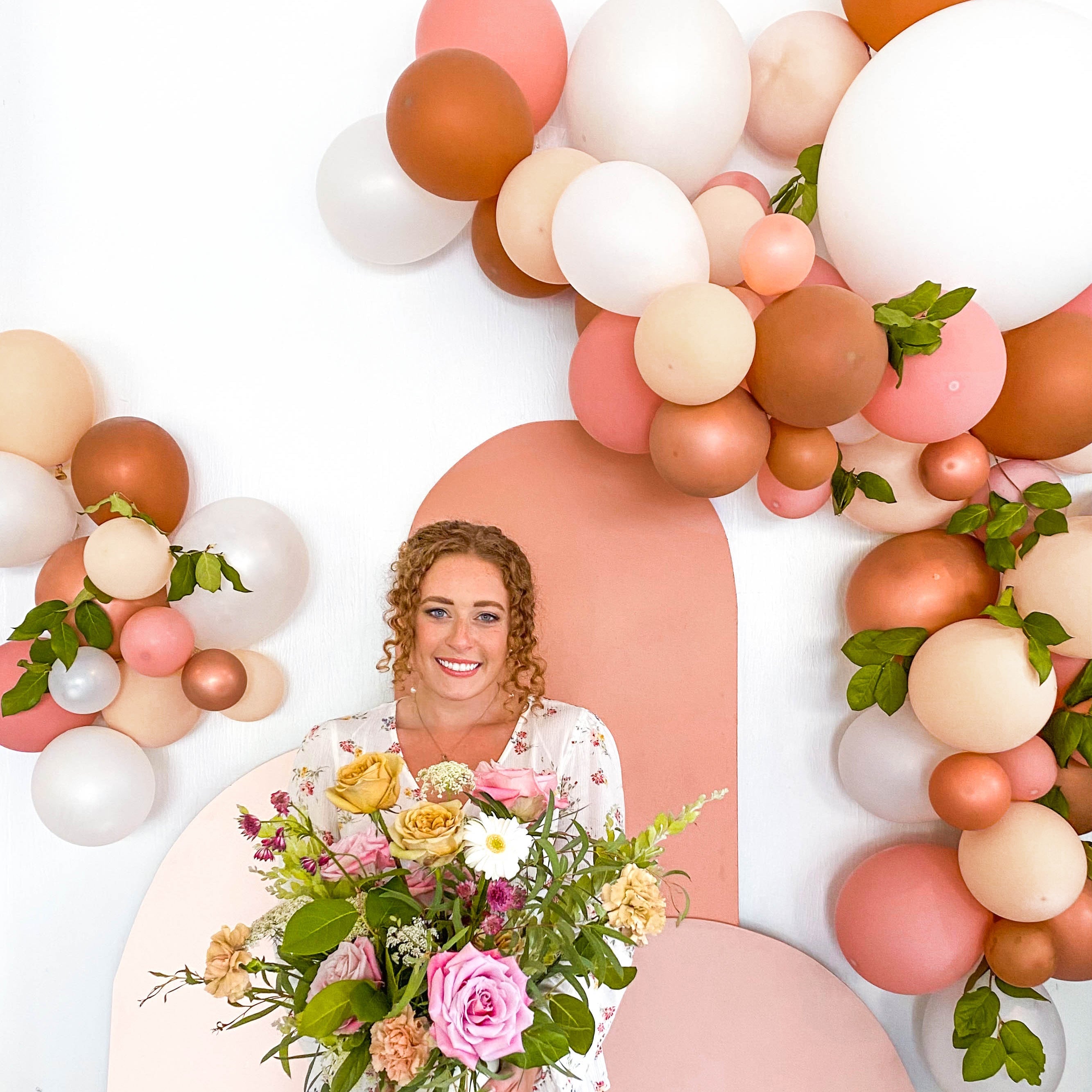 Woman holding a bouquet of flowers surrounded by a balloon arch on a white background Main image