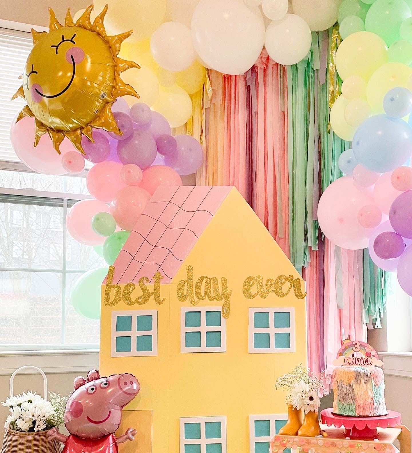 Decorative setup with a yellow house-shaped backdrop, balloons, and Peppa Pig figure.