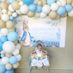 Baby celebrating a first birthday with a balloon arch and 'Peter Rabbit' themed backdrop.