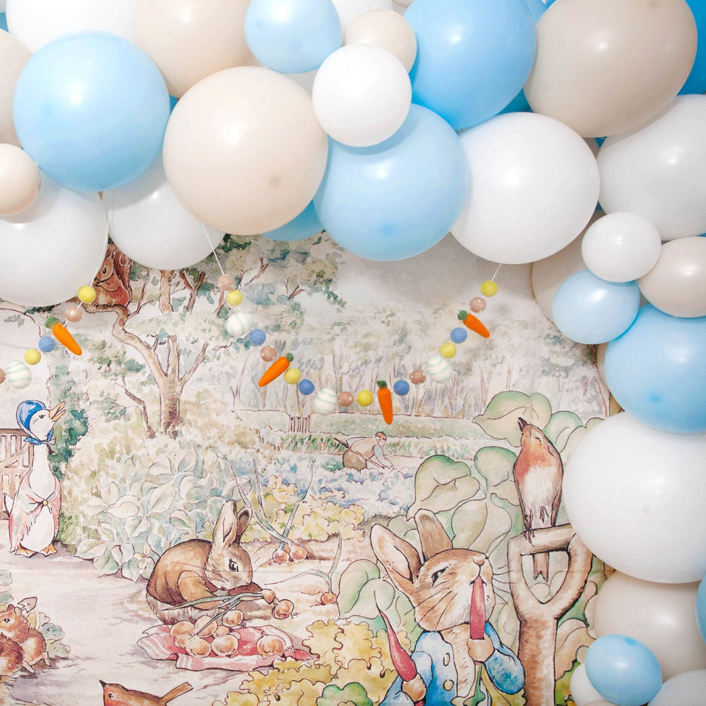 Balloon arch with blue, white, and beige balloons against a Peter Rabbit-themed backdrop.