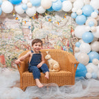 Child sitting on a wicker chair with a rabbit figurine, surrounded by colorful balloons and a children's book-themed backdrop.