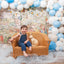 Child sitting on a wicker chair with a rabbit figurine, surrounded by colorful balloons and a children's book-themed backdrop.