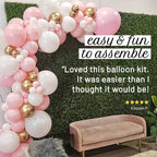 Balloon arch with pink, white, and gold balloons against a green wall with a couch underneath.