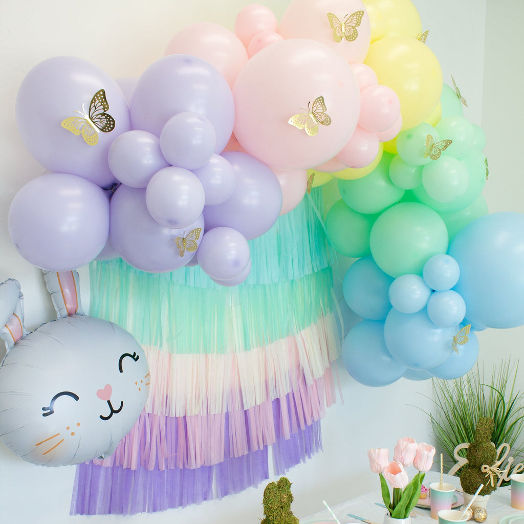 Pastel-colored balloon arch with tassels and decorative elements on a white wall.