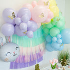Pastel-colored balloon arch with tassels and decorative elements on a white wall.