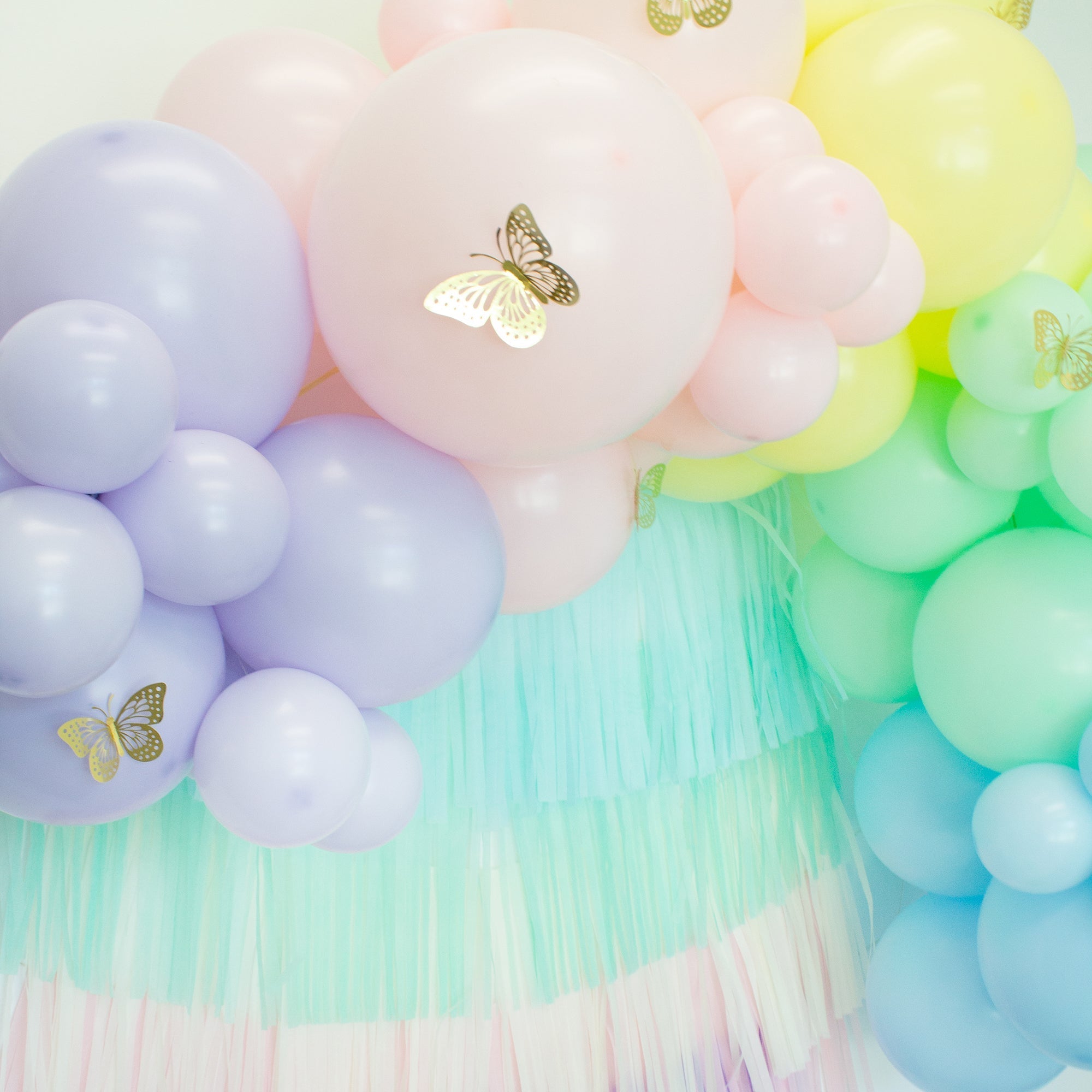 Pastel-colored balloon arch with tassels and butterfly decorations.