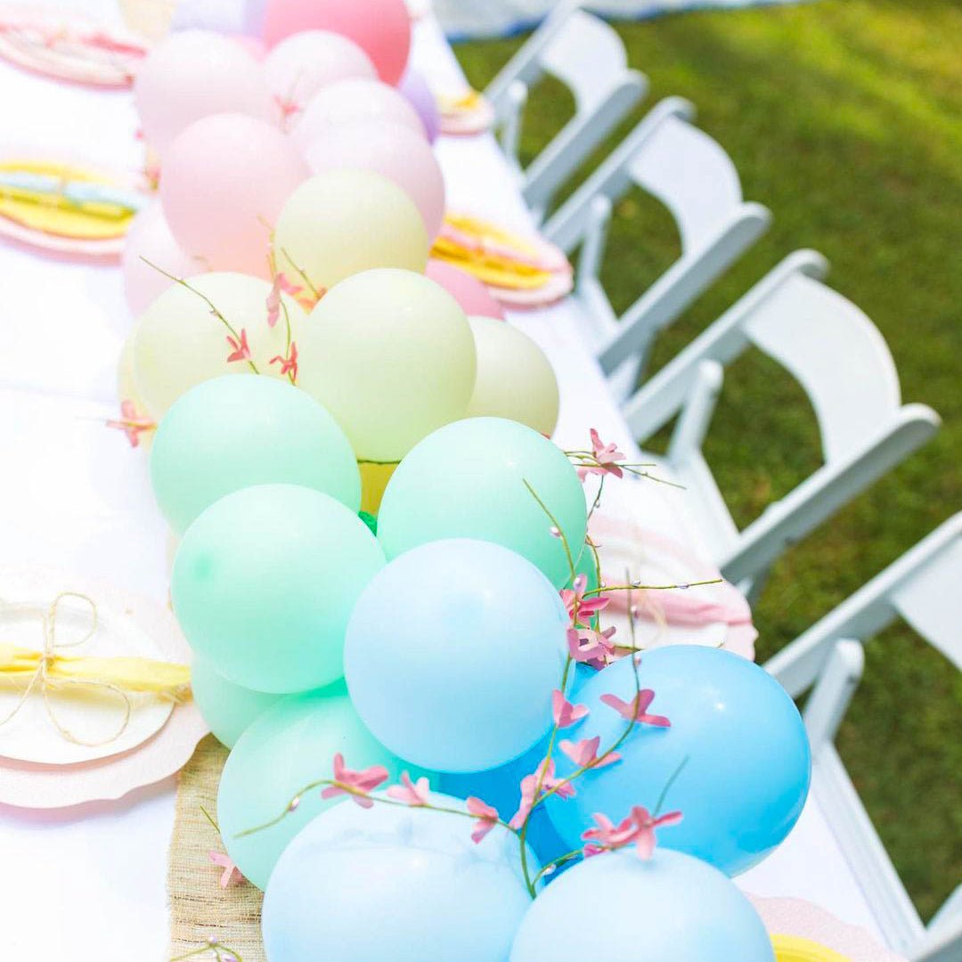 Decorative arrangement of pastel balloons and ribbons on a chair with outdoor setting.