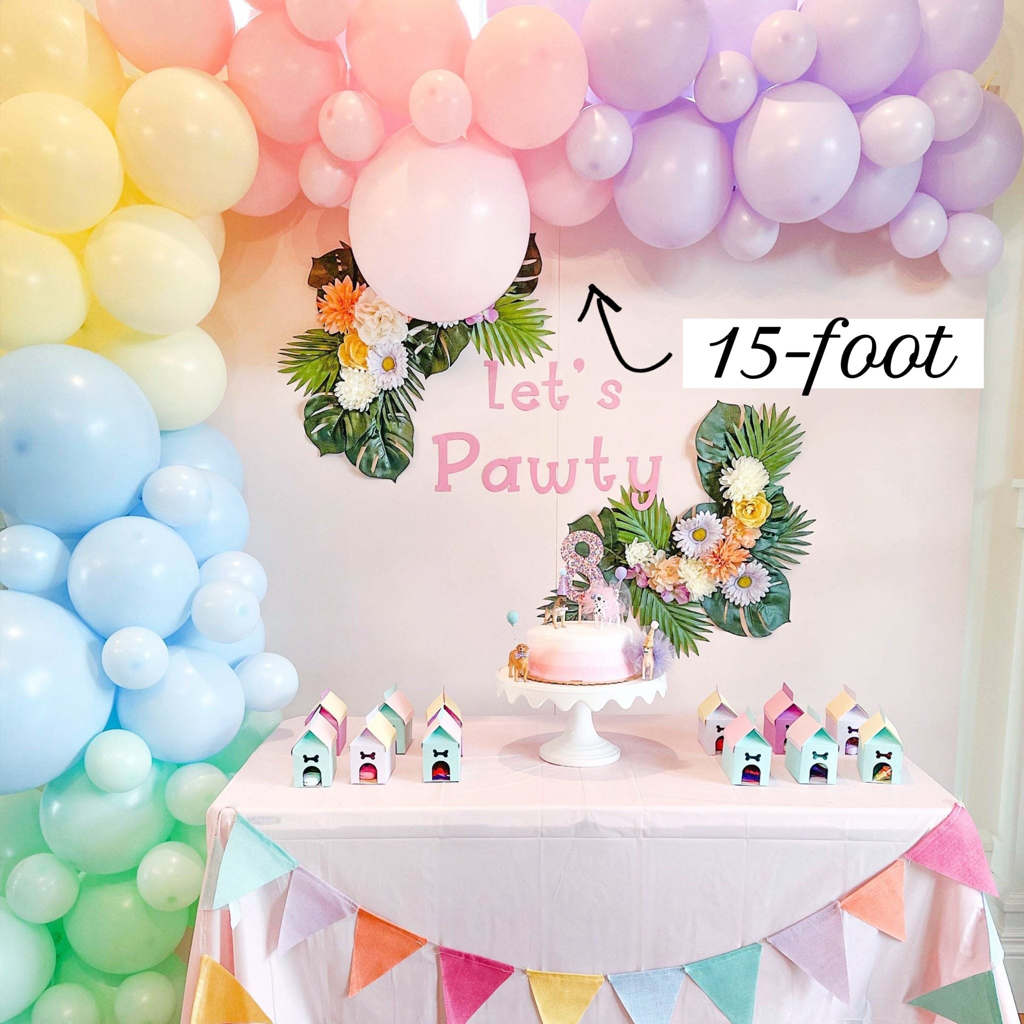 Birthday party setup with colorful balloons, cake, and decorations against a white wall.