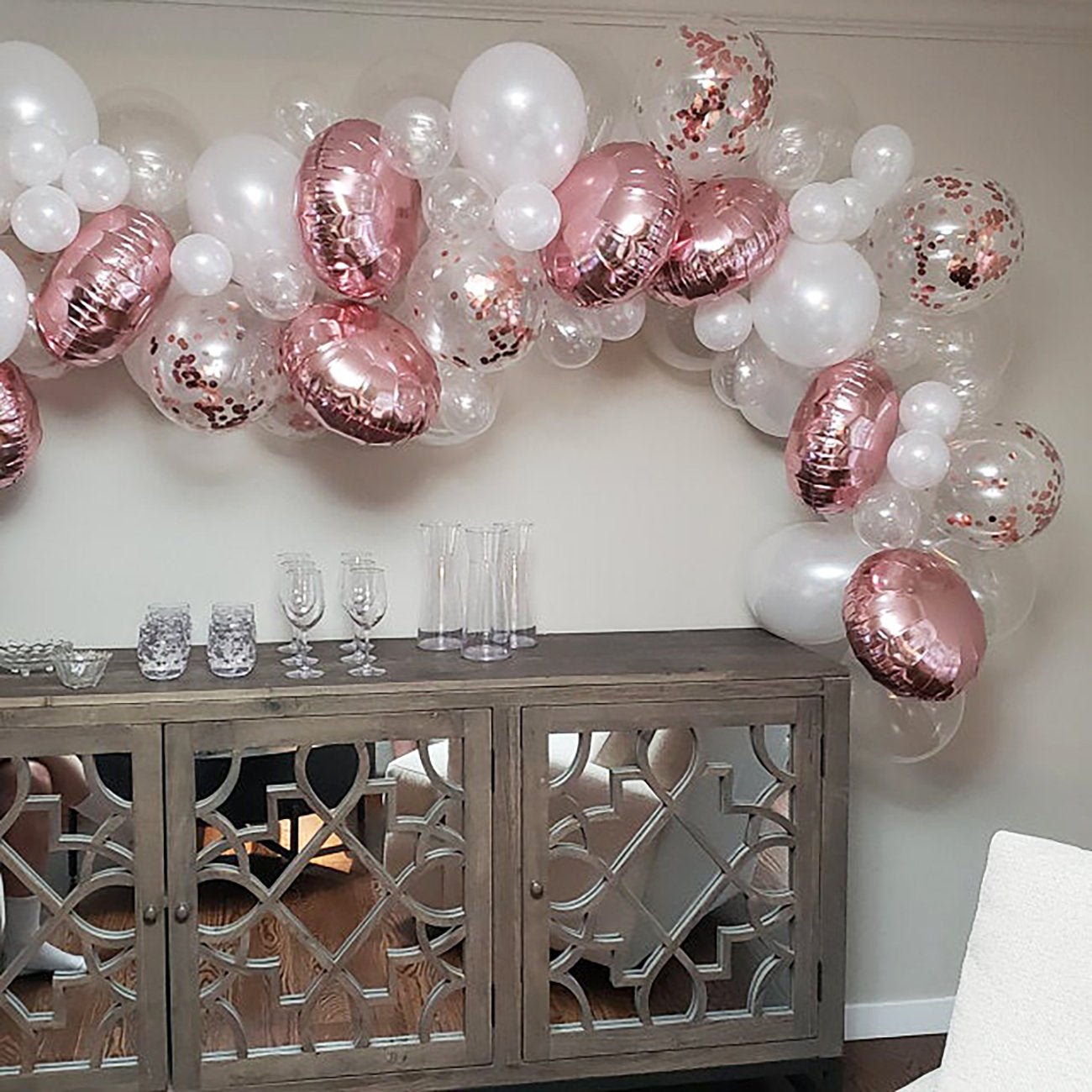 Balloon arch with pink and white balloons above a wooden console table.