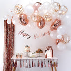 Birthday party setup with balloons, cake, and decorations on a white wall.