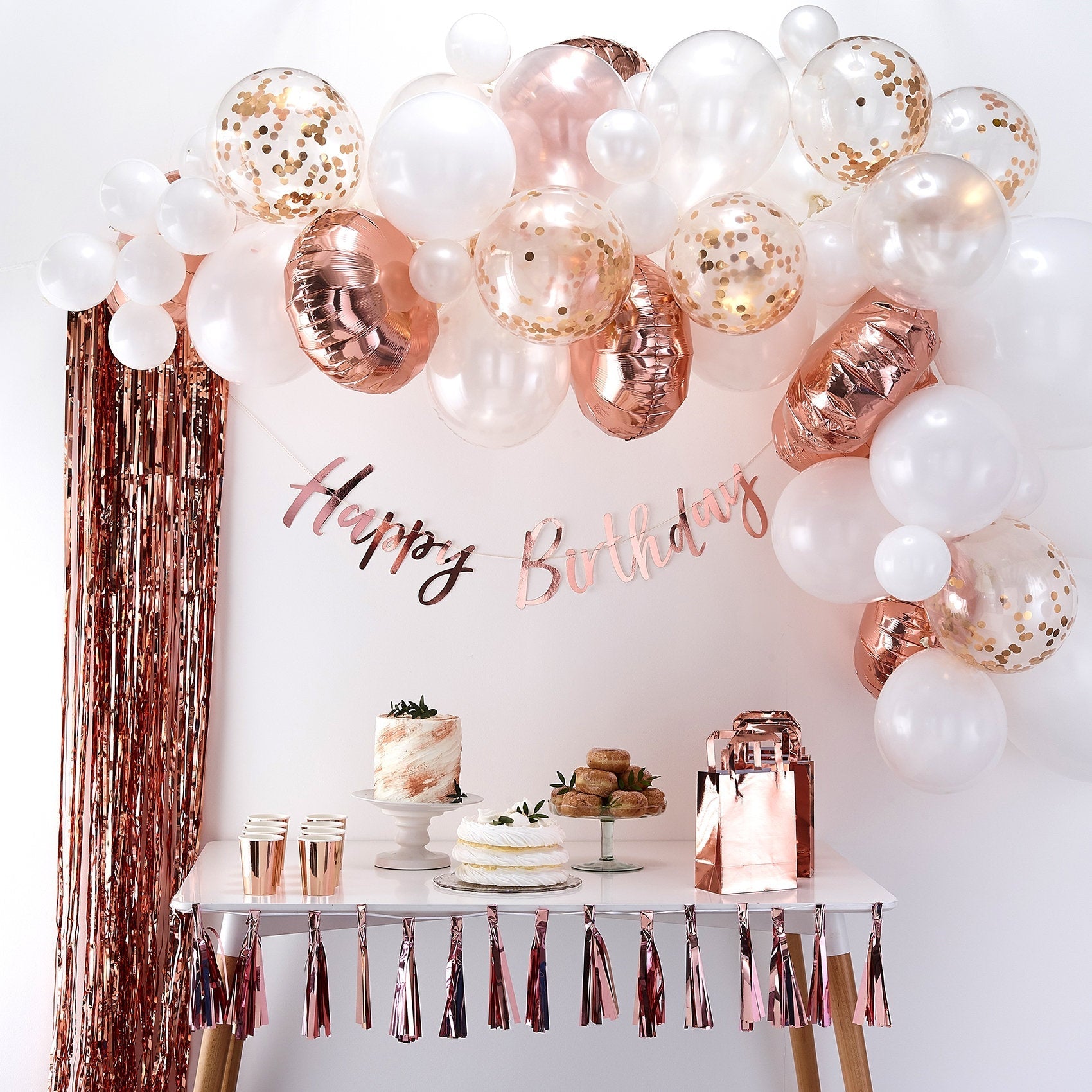 Birthday party setup with balloons, cake, and decorations on a white wall.