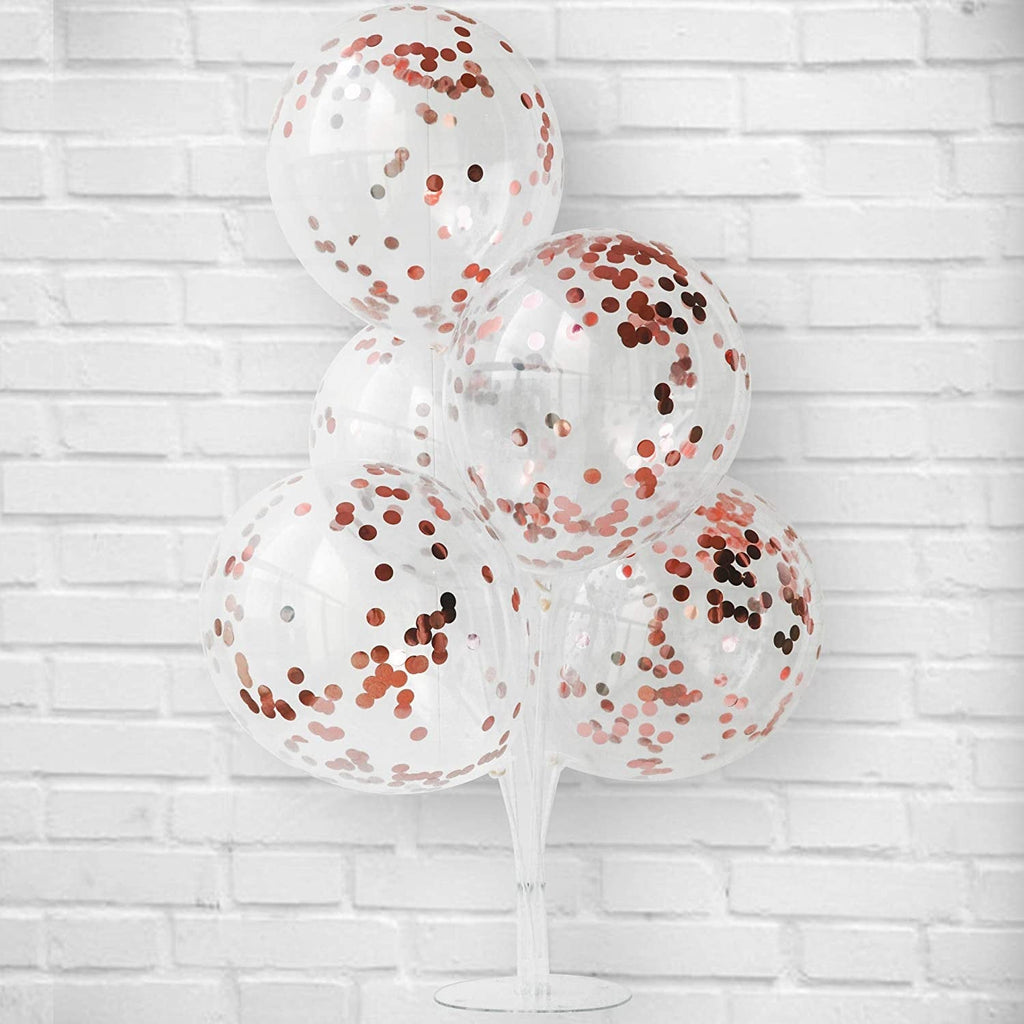 Clear balloons with rose gold confetti against a white brick wall background