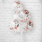 Clear balloons with rose gold confetti against a white brick wall background