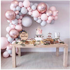 Decorative table with balloons and baby shower decorations against a light pink wall.