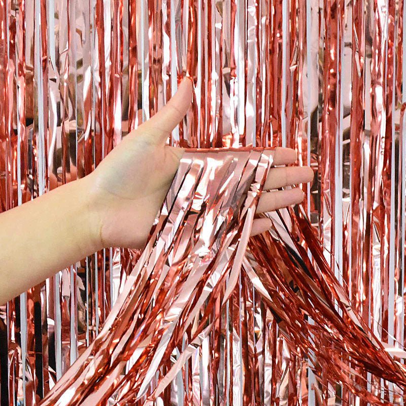 Hand holding rose gold tinsel curtain backdrop against a rose gold tinsel curtain
