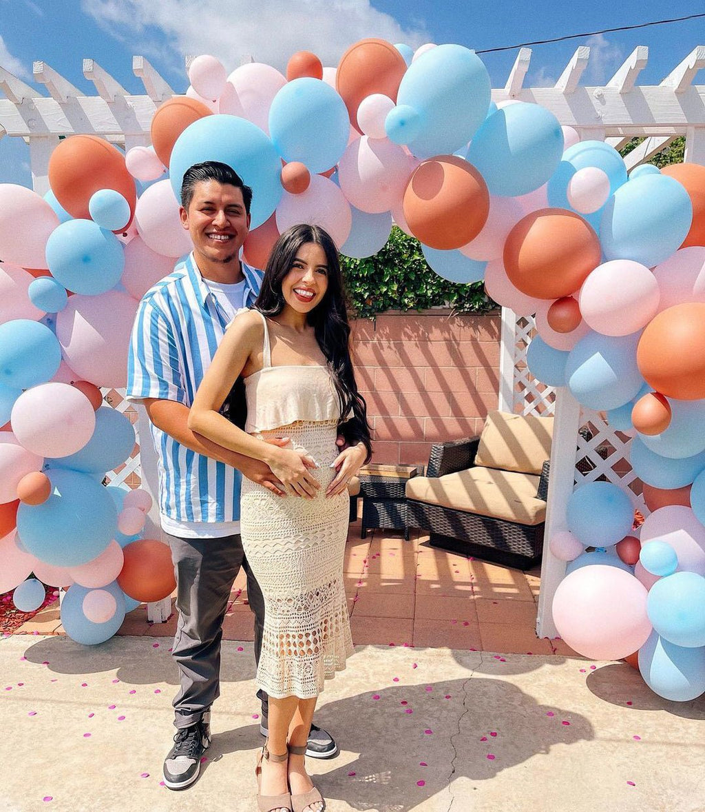 Couple standing in front of a colorful balloon archway with a white pergola in the background.