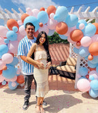 Couple standing in front of a colorful balloon archway with a white pergola in the background.
