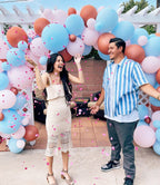 Couple standing in front of a colorful balloon arch with confetti