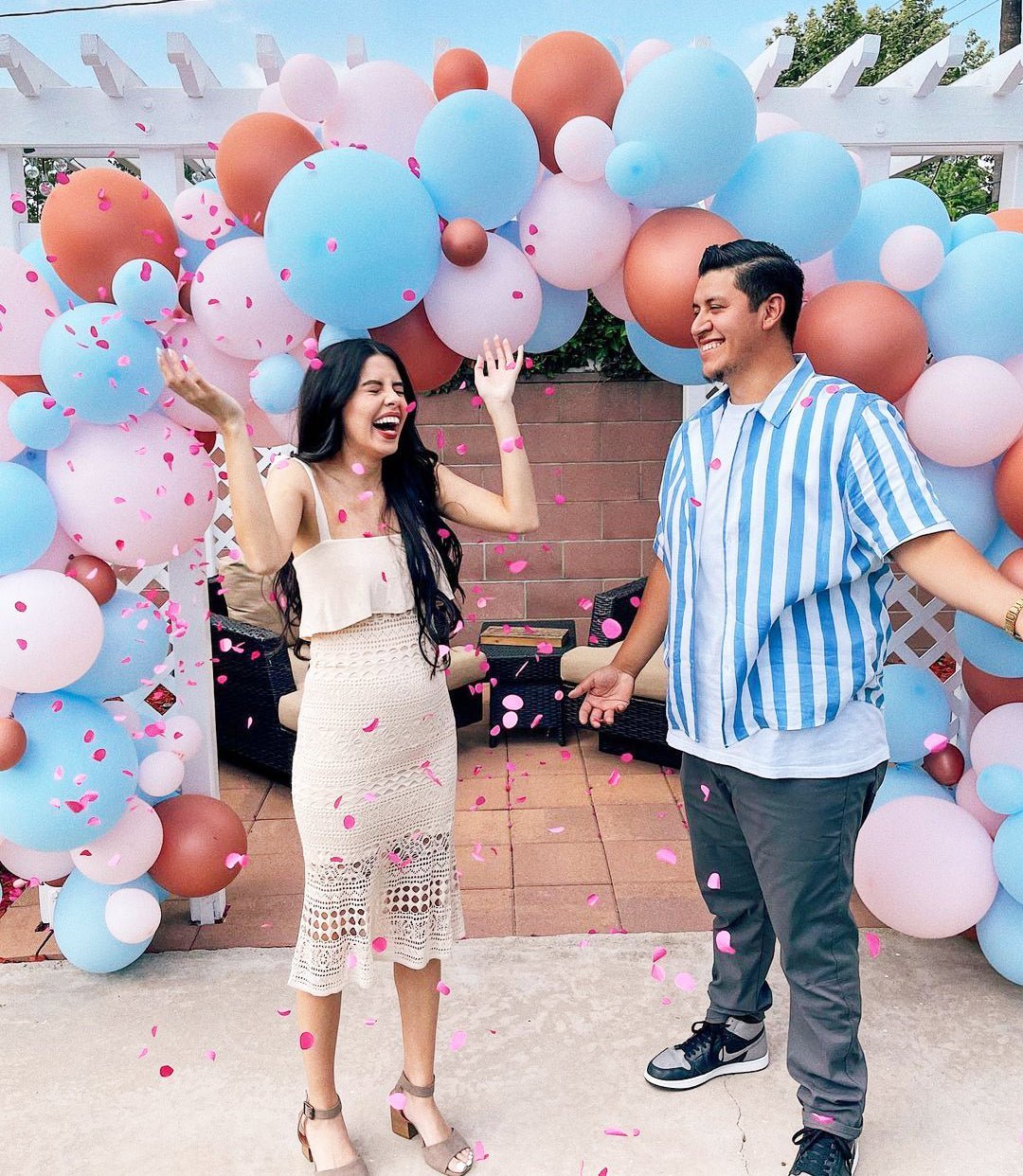 Couple standing in front of a colorful balloon arch with confetti