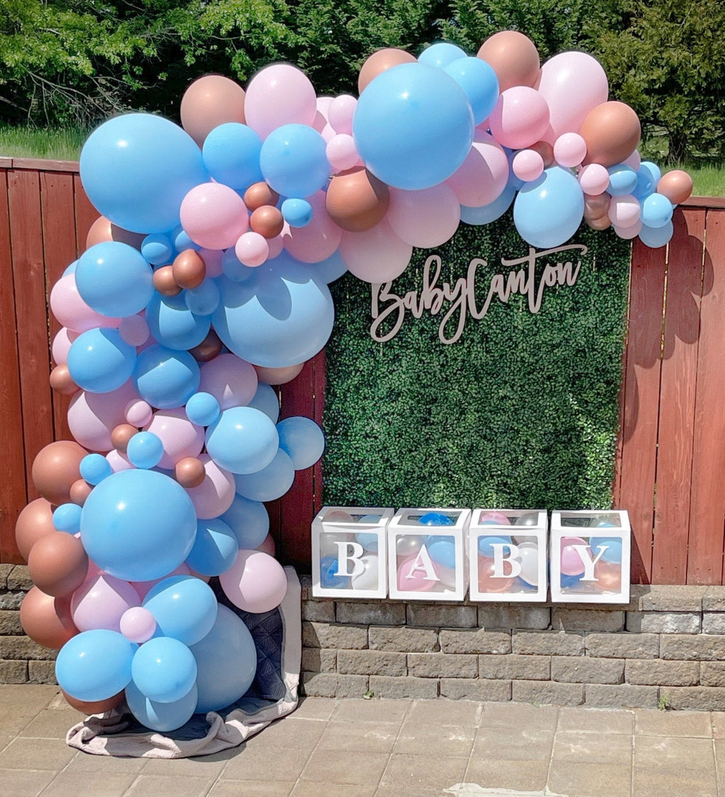 Balloon arch with blue, pink, and brown balloons in front of a green foliage backdrop with 'Baby Canton' text.