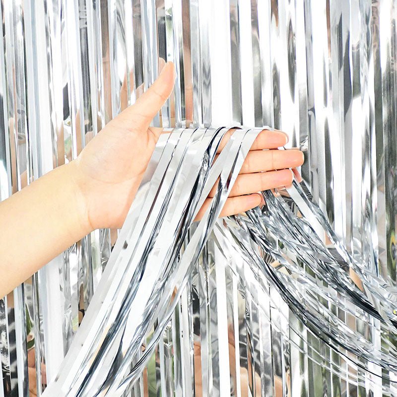 Person holding silver tinsel against a blurred outdoor background