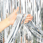Person holding silver tinsel against a blurred outdoor background