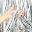 Person holding silver tinsel against a blurred outdoor background
