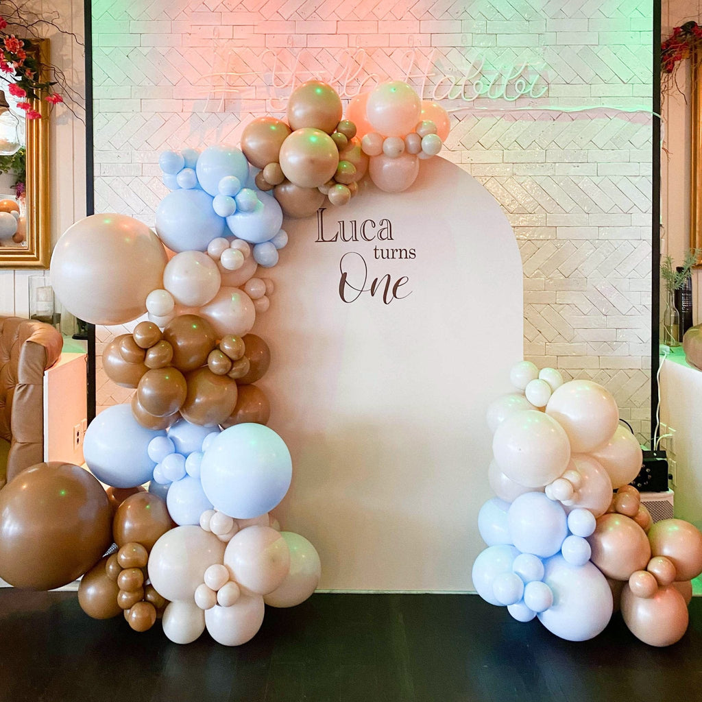 Balloon arch with pastel colors in front of a wall with 'Luca turns One' text.