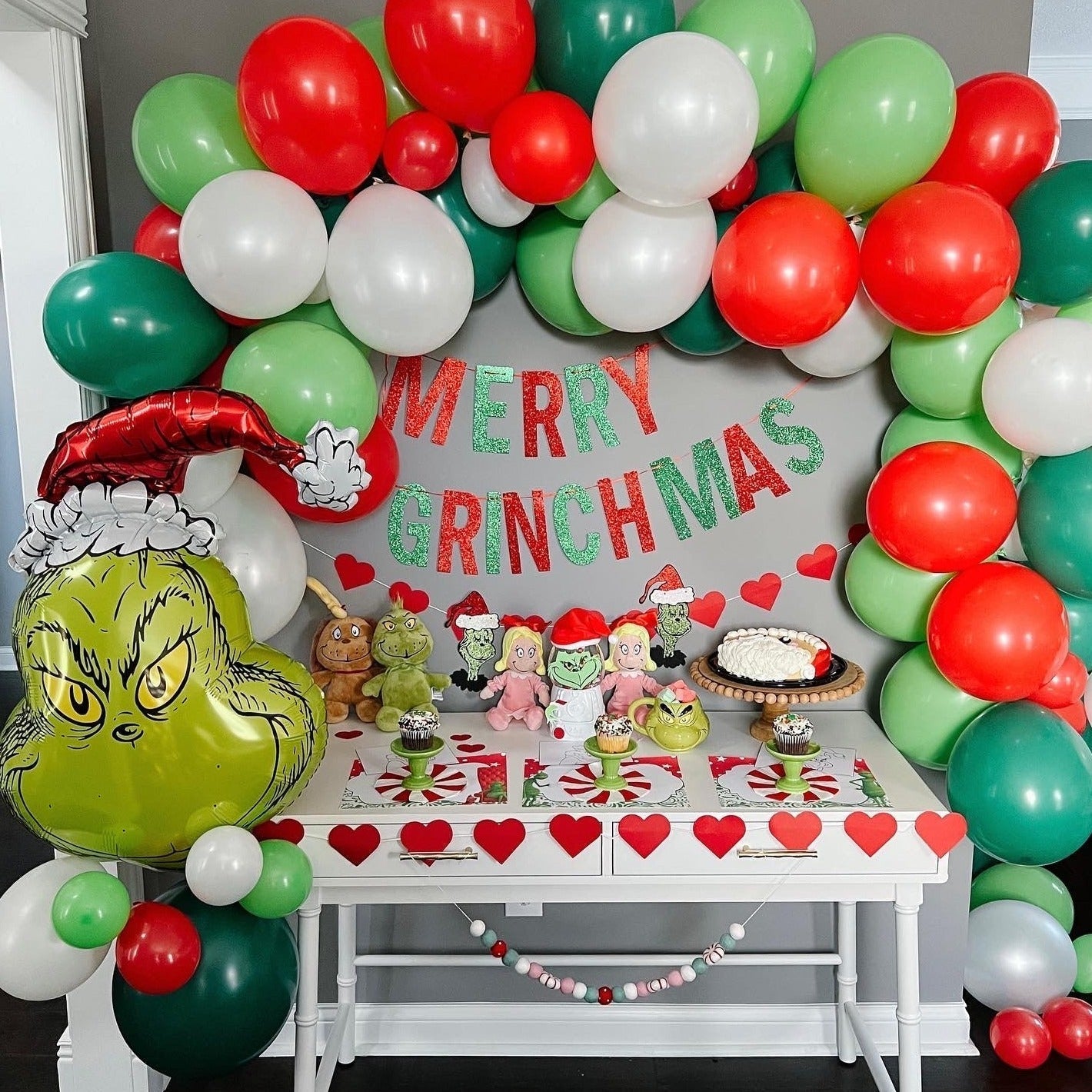 Decorated room with balloons, 'Merry Grinchmas' sign, and Grinch-themed table setting.