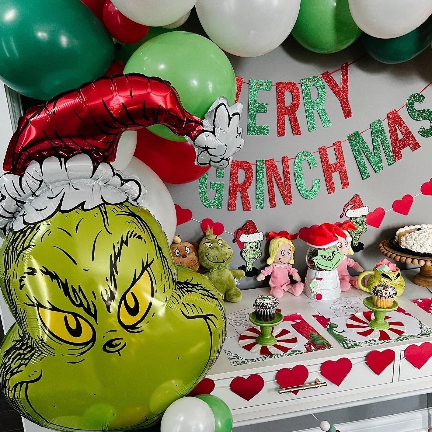 Decorative setup with 'Merry Grinchmas' banner, balloons, and festive decorations.