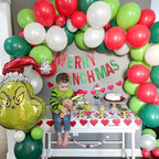 Child in a festive setting with balloons, 'Merry Christmas' sign, and Grinch balloon.
