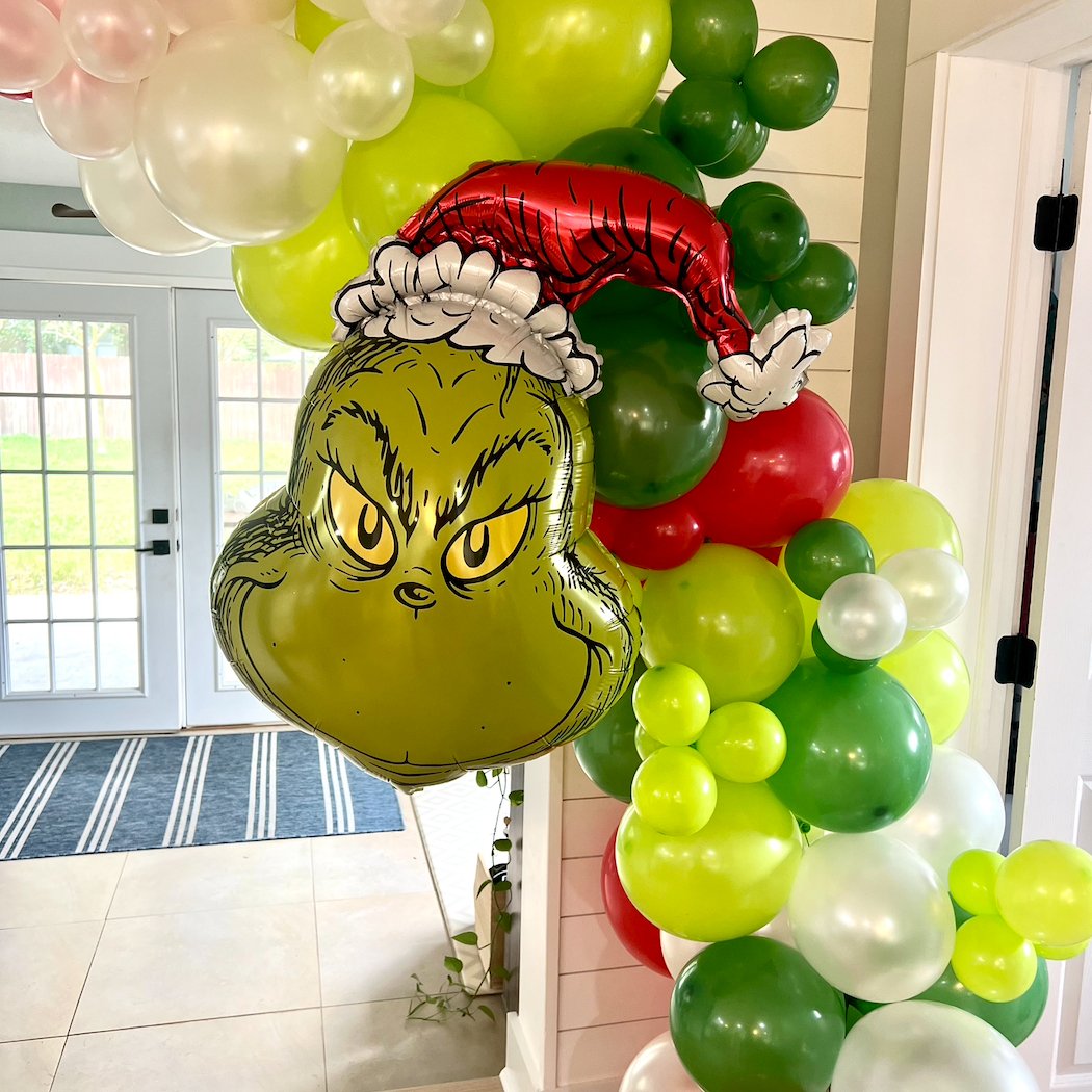 Balloon arch with Grinch face and Santa hat balloons in a room.