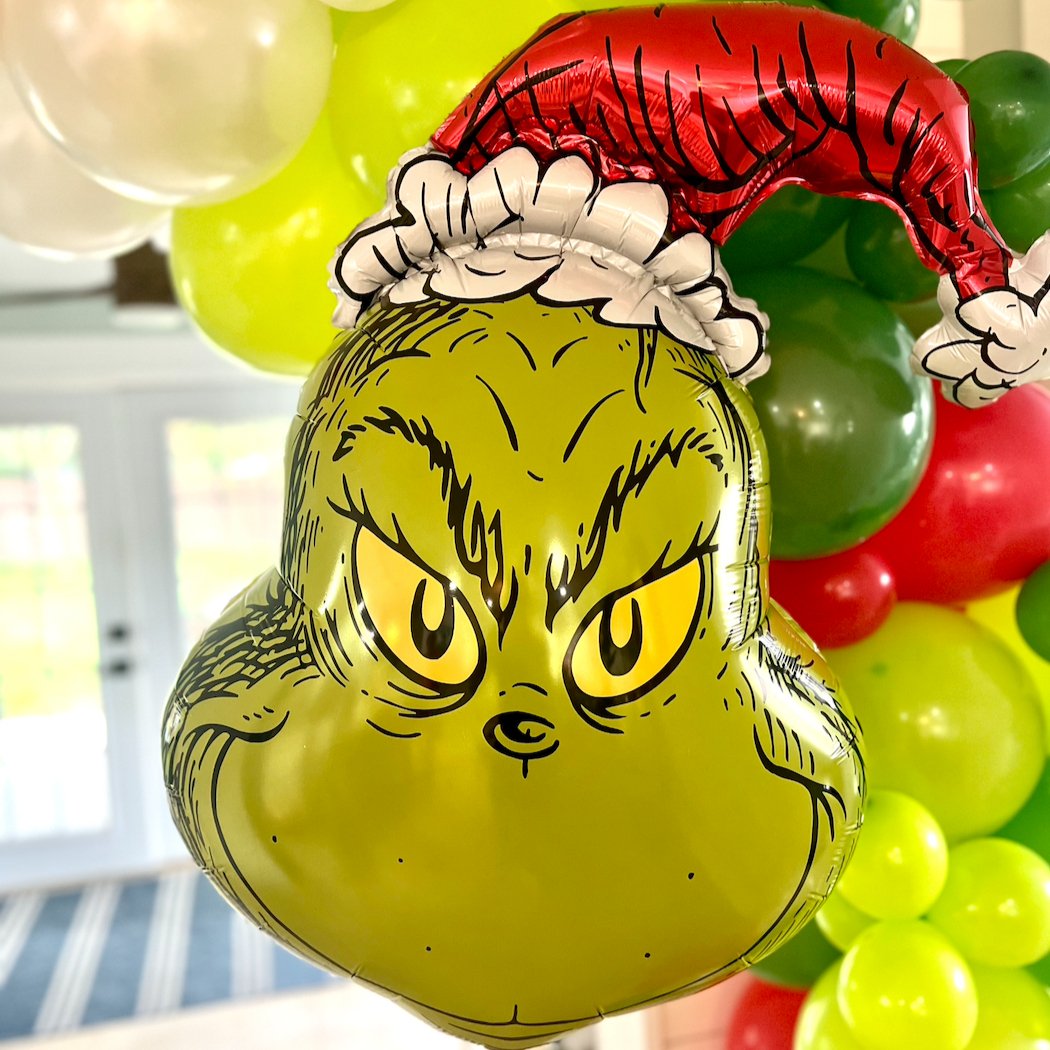 Balloon shaped like the Grinch with a red hat and white gloves, surrounded by other balloons.