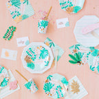 Party supplies with tropical palm leaf designs on a pink background