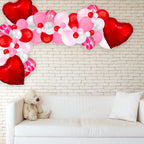 Heart-shaped balloons and a teddy bear on a white couch against a brick wall.