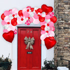 Decorative balloon arch with red, pink, and white balloons above a red door with a gold bow.