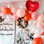 Decorative setup with balloons, wreath, and a sign in a festive setting.