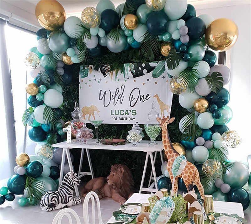 Birthday party setup with balloon arch, animal figurines, and 'Wild One' sign.