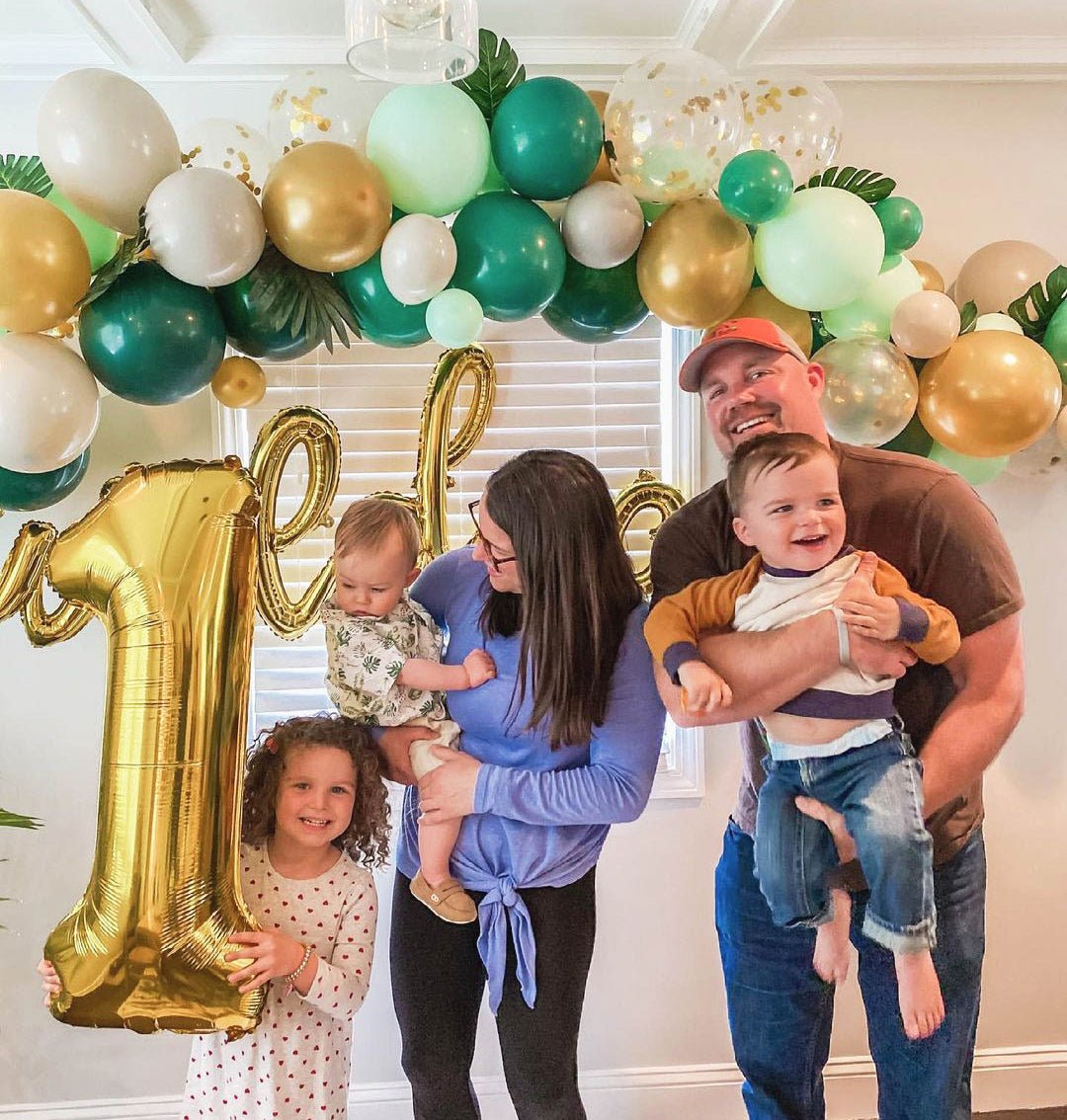 Family of five celebrating a child's first birthday with balloons and decorations.