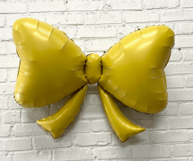Yellow bow-shaped balloon against a white brick wall background Main image
